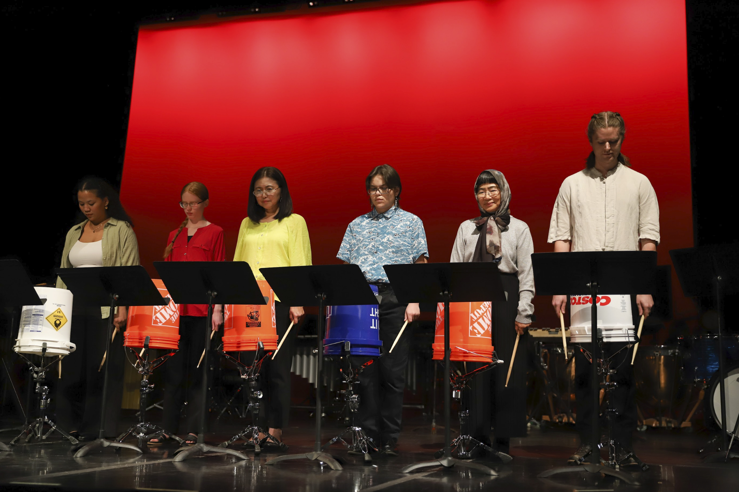 Photo of brightly clad members of the PCC Percussion Ensemble preparing to perform using five-gallon plastic buckets as their instrument.