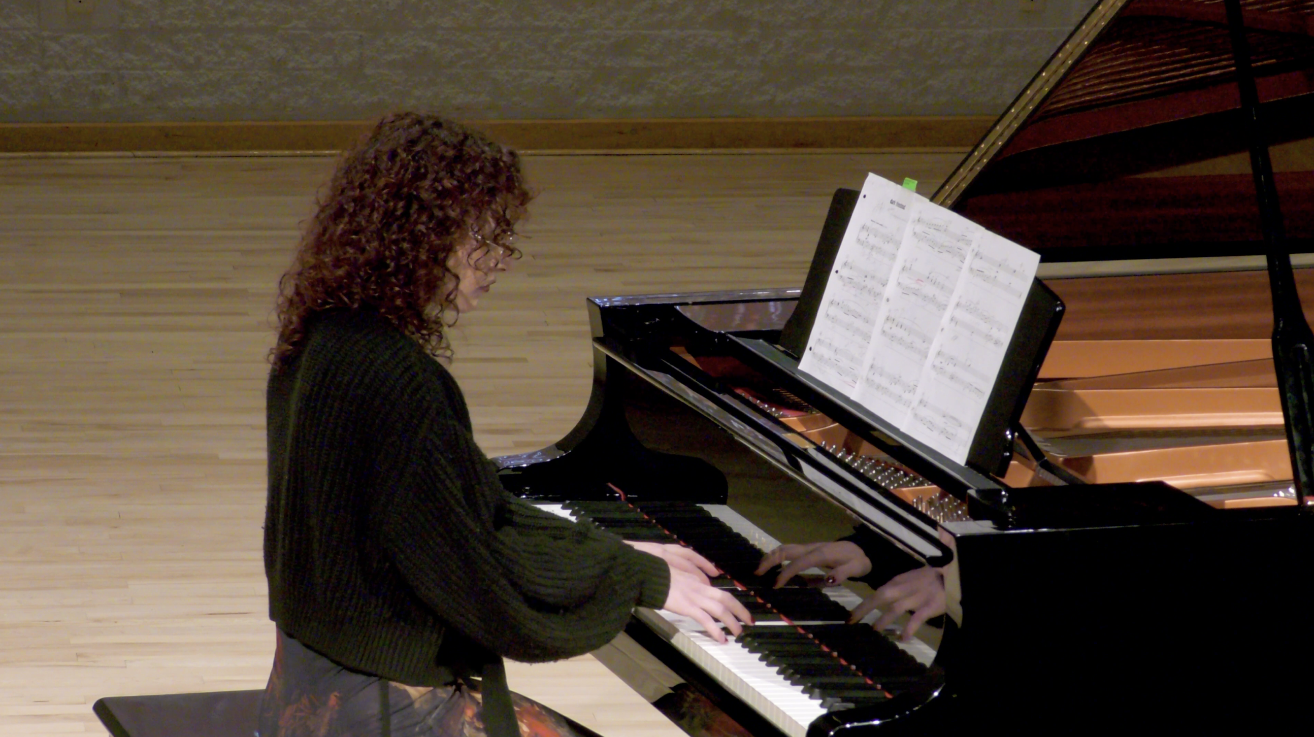 Photo of a woman with curly hair playing the piano in the Recital Hall.