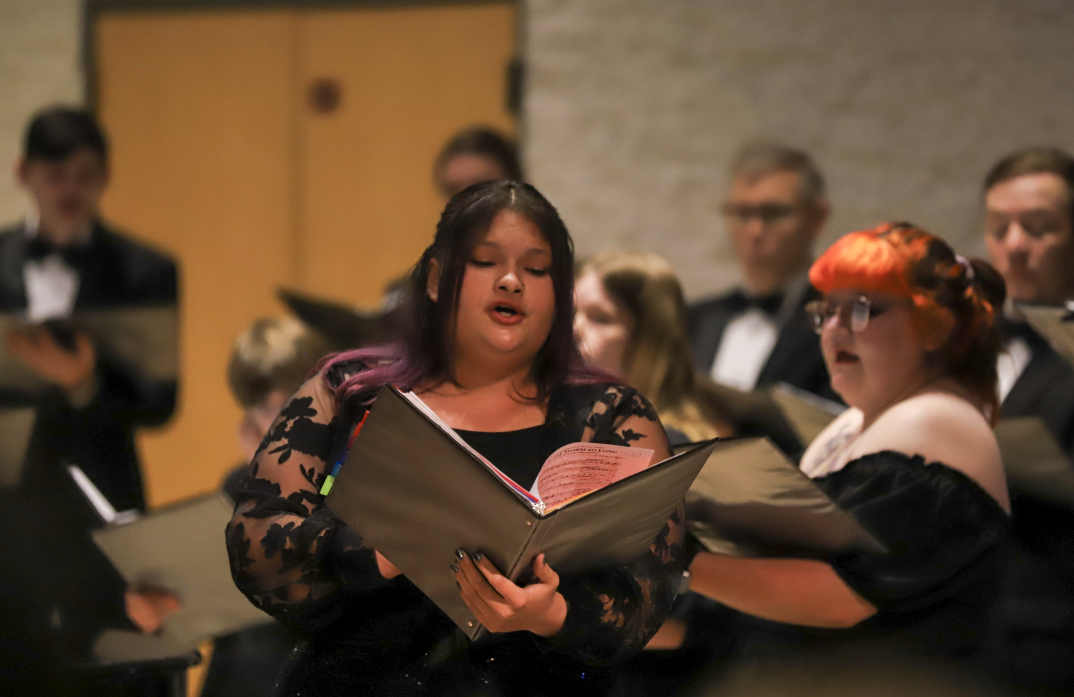 Photo of a woman soloist singing with a choir behind her.