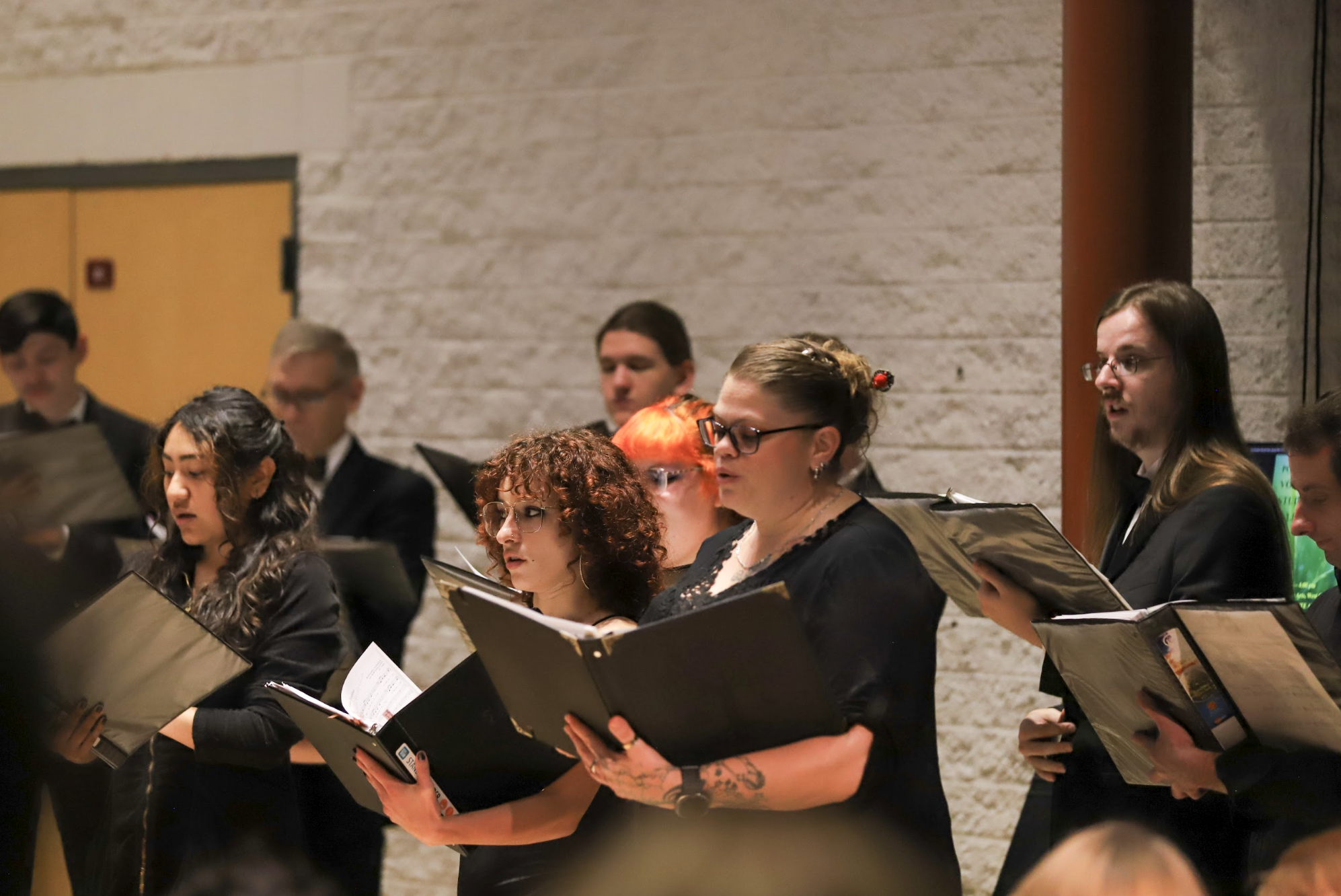 Photo of several male and female students in black singing in the Recital Hall.