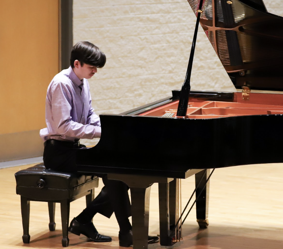 Photo of a dark-haired male student in a lavender shirt playing the piano in the Recital Hall.