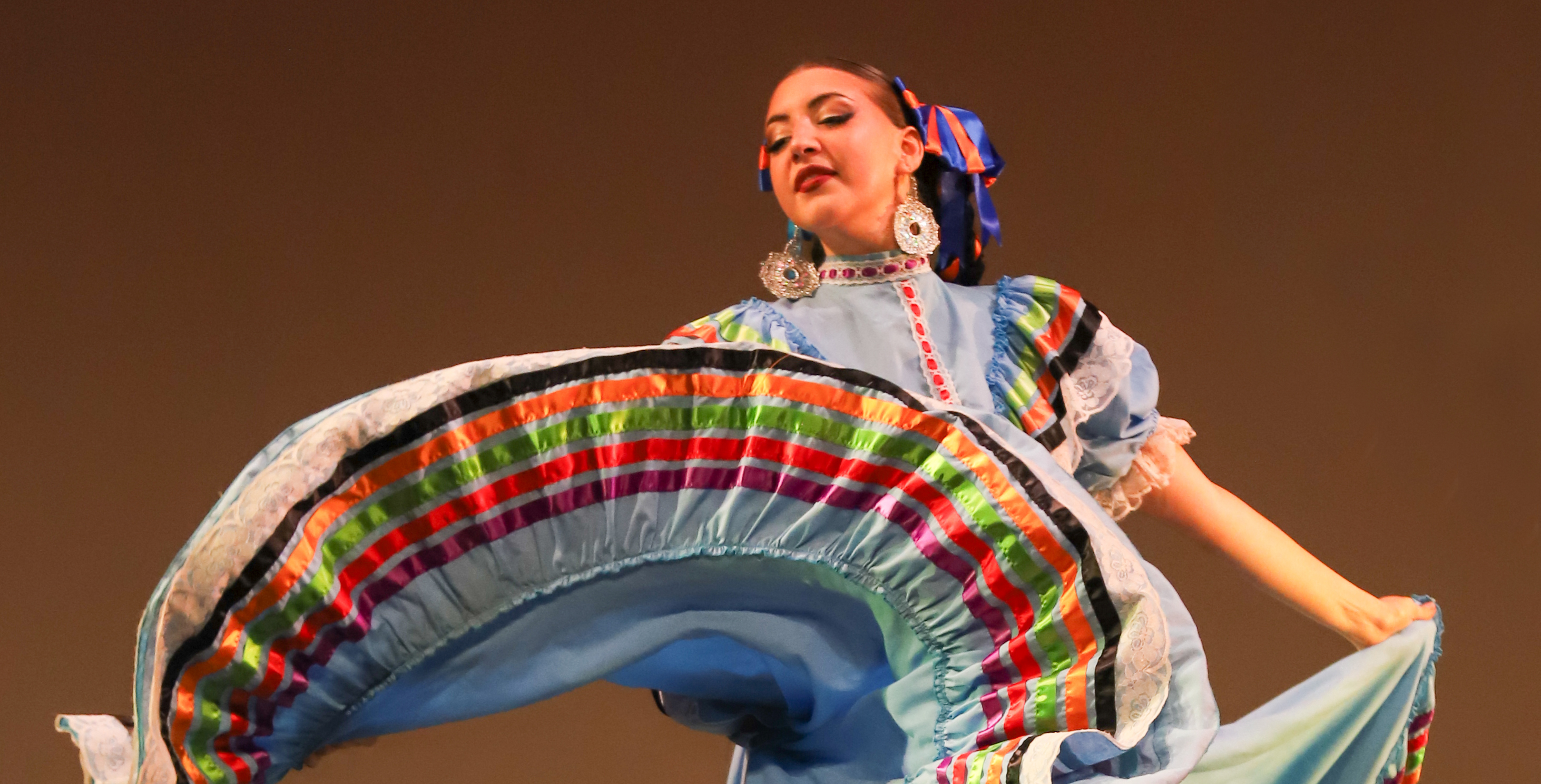 Closeup photo of a folklorico dancer in blue sweeping her ribboned skirt out to the side in a graceful arc.